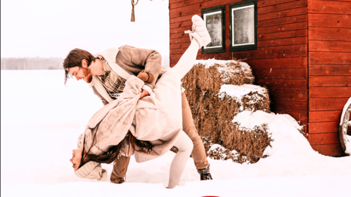 Romantic couple in a playful and old fashioned dip pose while playing in the snow infront of a red barn. 