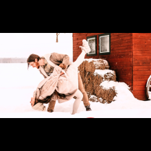 Romantic couple in a playful and old fashioned dip pose while playing in the snow infront of a red barn. 